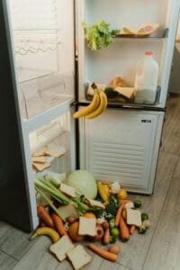 Ein geöffneter Kühlschrank. Lebensmittel fallen heraus und symbolisieren die Lebensmittelverschwendung